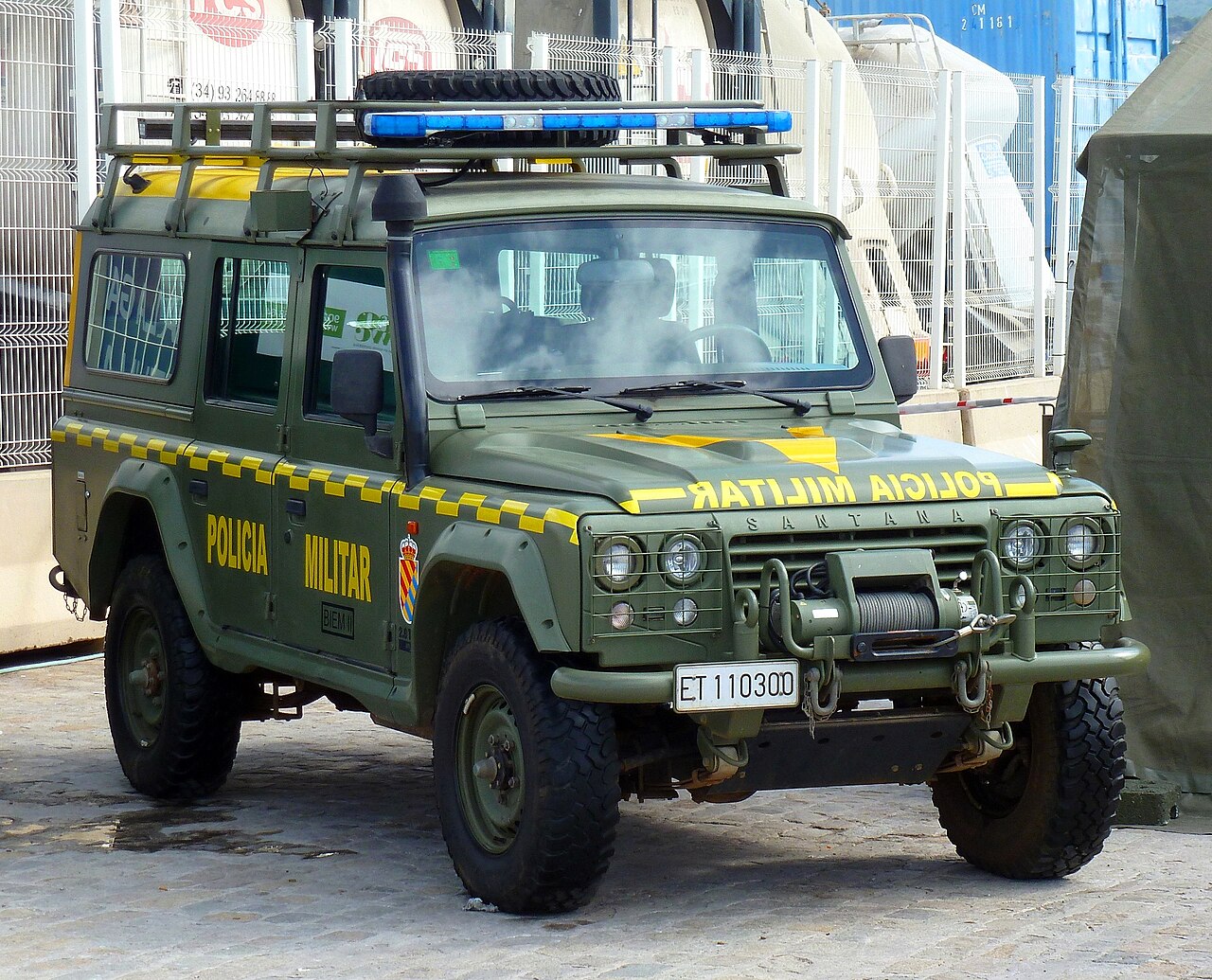 Military police Aníbal station wagon of the Unidad Militar de Emergencias (BIEM I), ET 110300 — yellow 'POLICIA MILITAR' lettering, chequered waist flash and blue light bar. A station wagon rather than the soft top