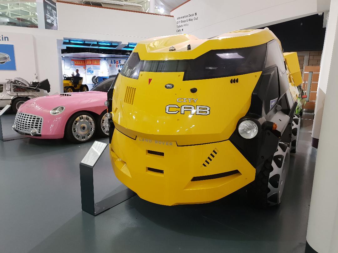Front view showing the sculpted yellow body, enclosed wheels and Land Rover badging, British Motor Museum, 2023