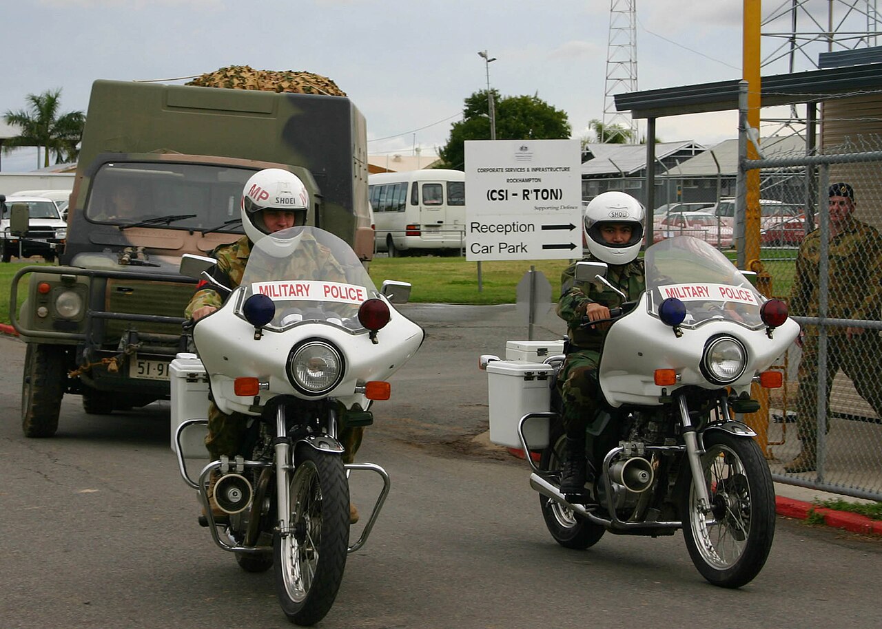 Canvas-topped Australian Army Perentie 110 4x4 (ARN 51-9xx, the RFSV/4x4 fleet number series) behind military police motorcycles at Camp Rocky, Queensland, during Talisman Sabre 2005